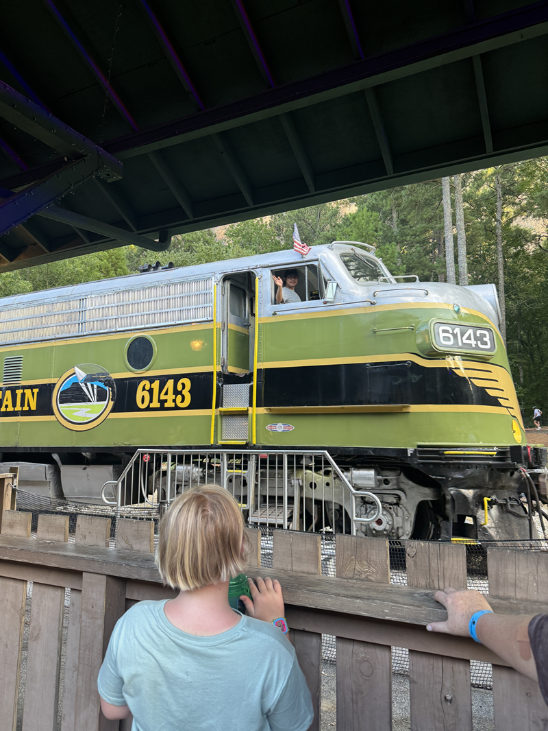 Stone Mountain Scenic Railroad train with green engine train. Conductor is waving while a young girl looks on. Weekend Getaway to Stone Mountain